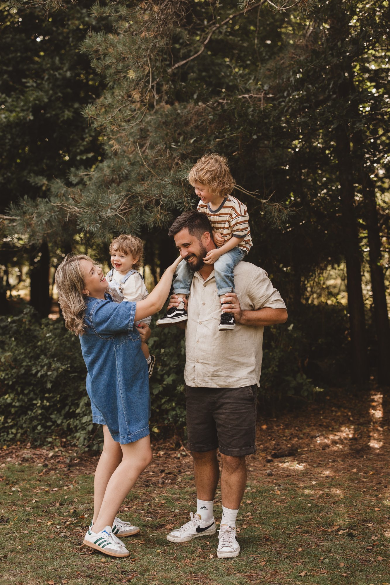 Parents holding their two young sons in a woodland clearing, candid family moment