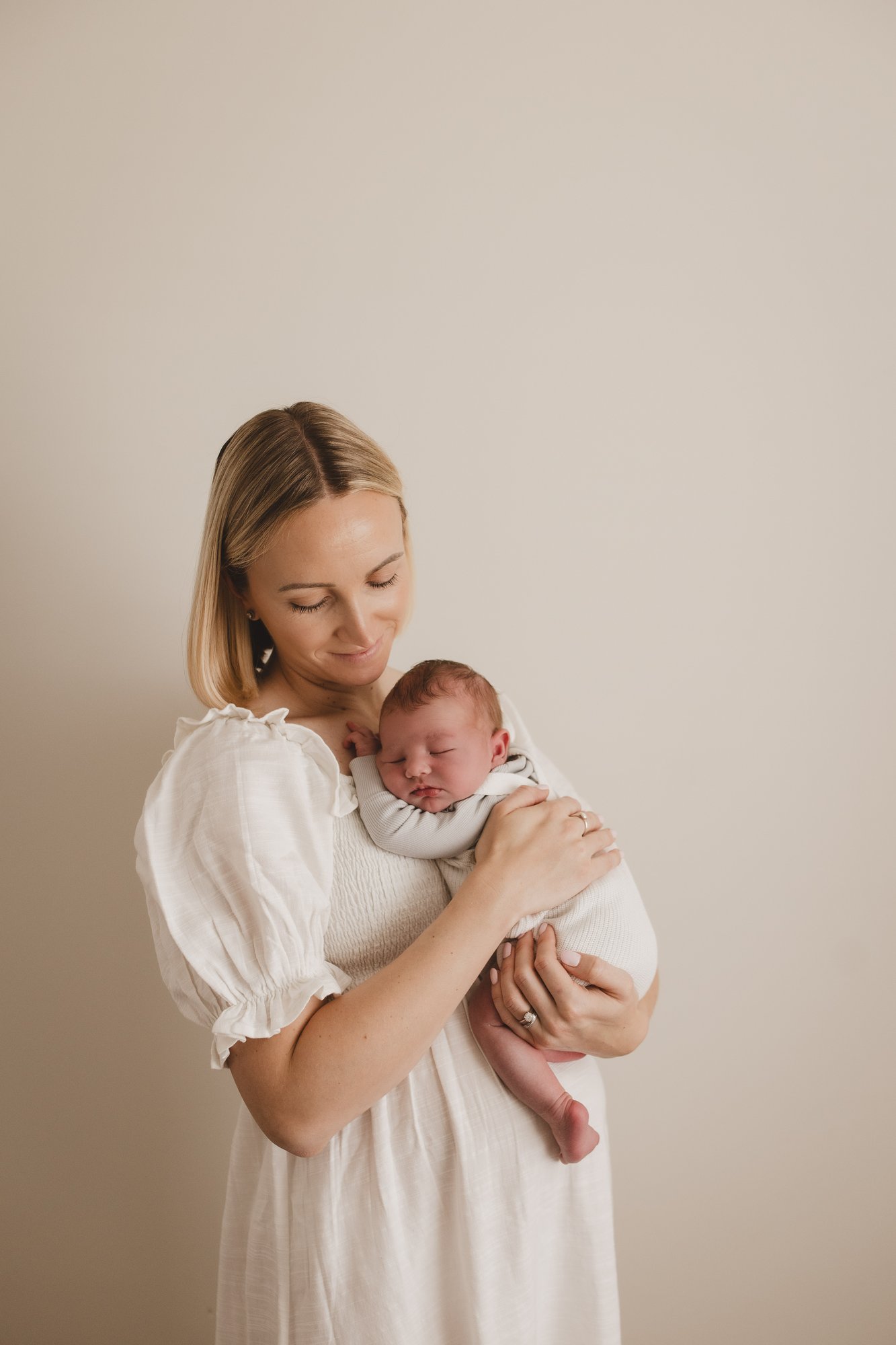 New mum in a white dress softly cradling her sleeping newborn baby
