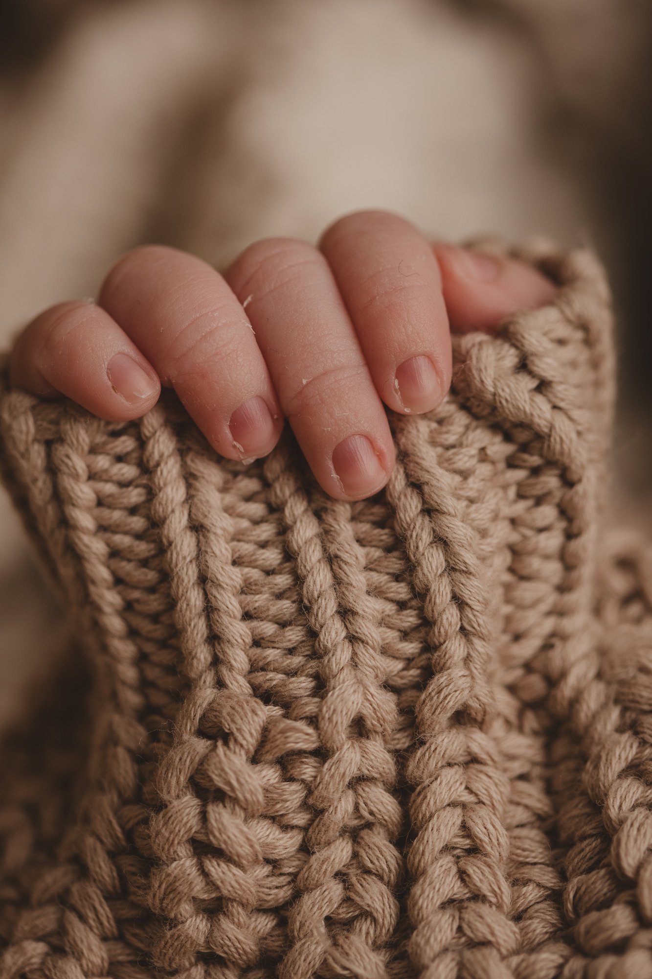 Detail of a newborn baby's tiny hand resting on a chunky knit blanket