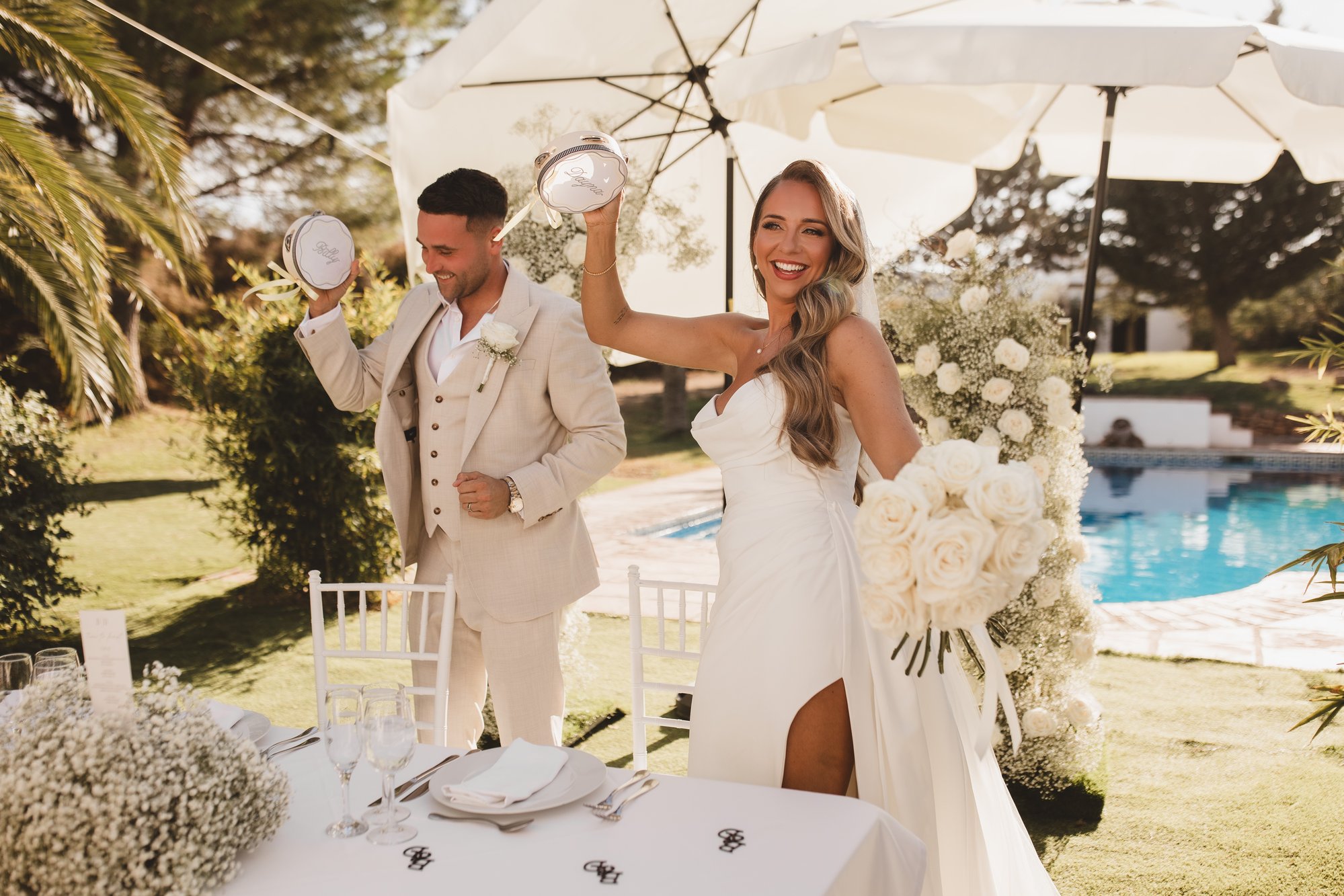 Bride raising a personalised tambourine in joyful celebration with her groom at an outdoor wedding reception
