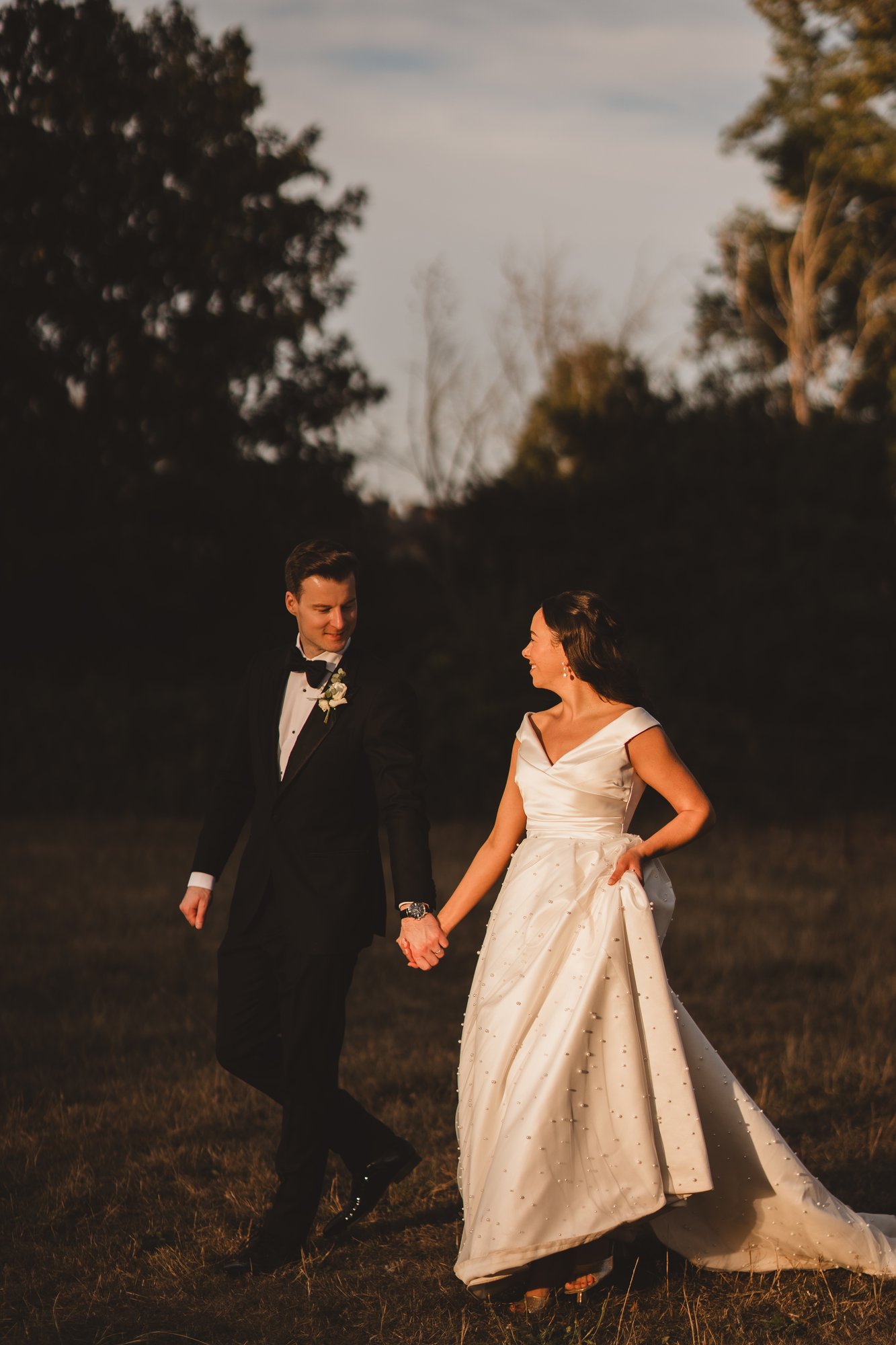 Bride and groom holding hands at golden hour in an open field
