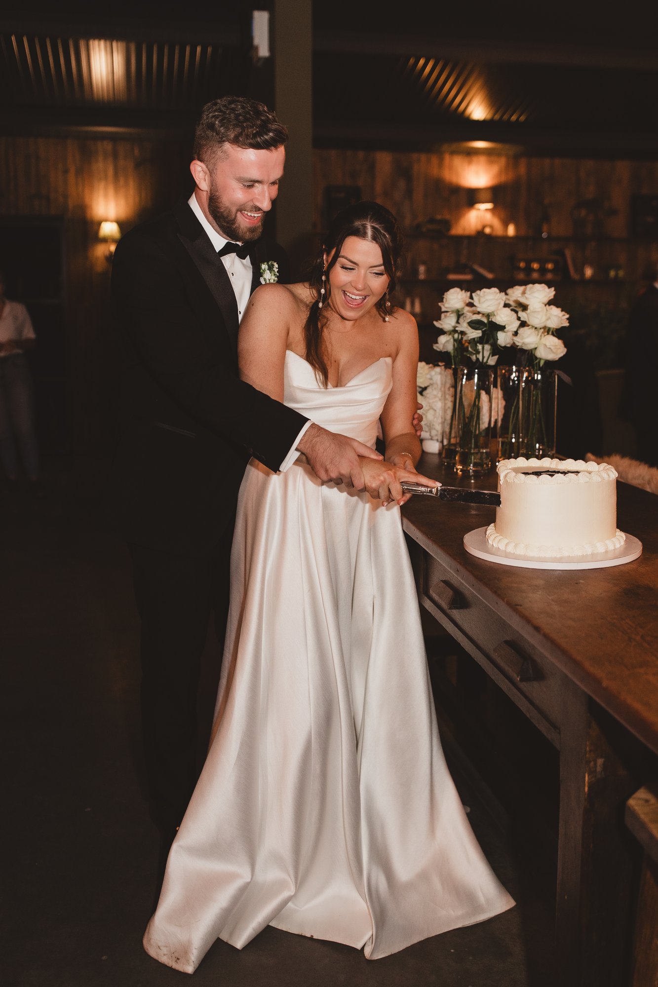 Bride and groom cutting their wedding cake at a candlelit barn reception