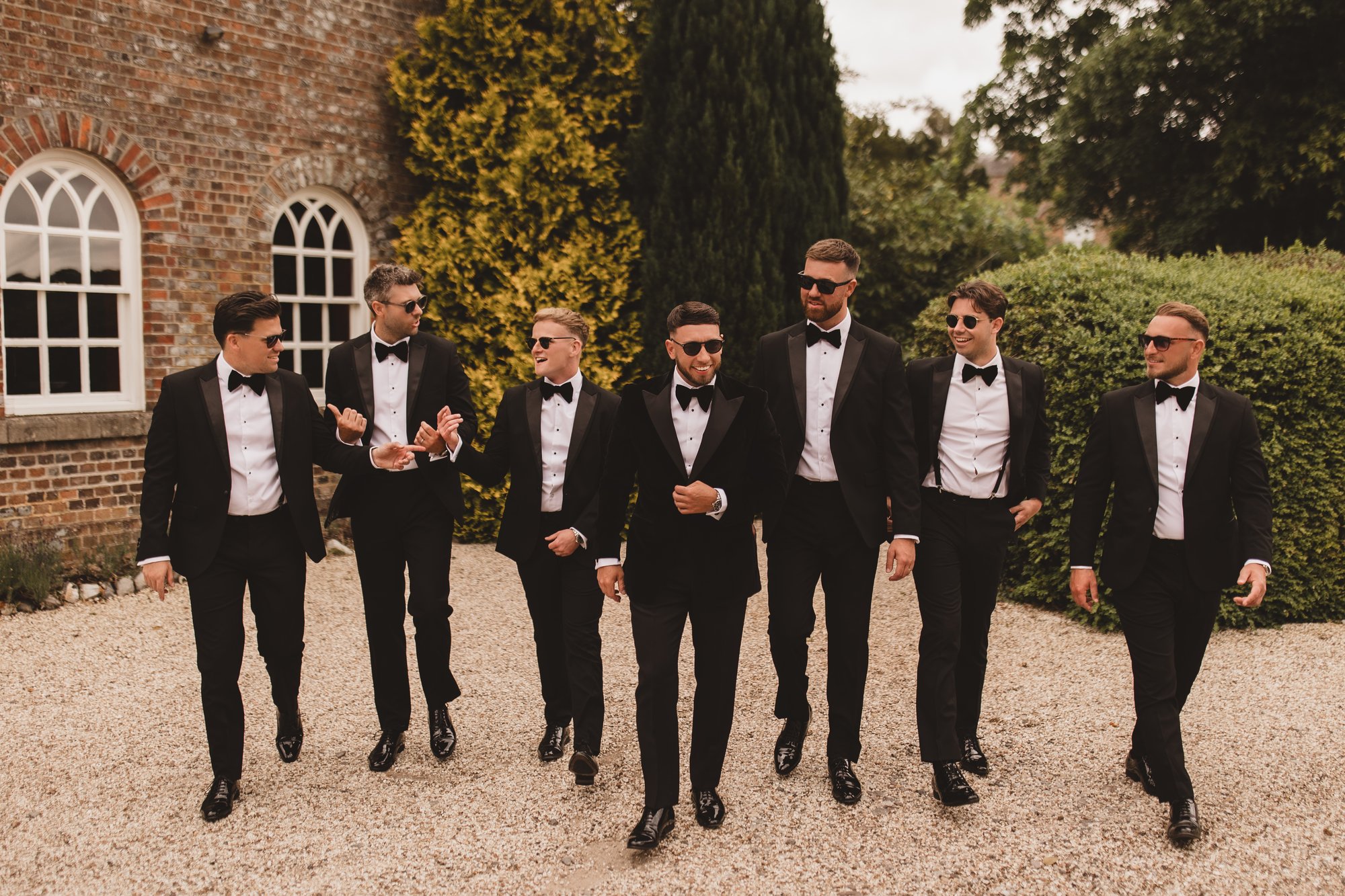 Groomsmen in black tie walking together in front of a country wedding venue